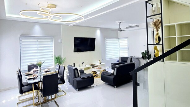 A modern living room with a dining area, a staircase, and a TV mounted on the wall.