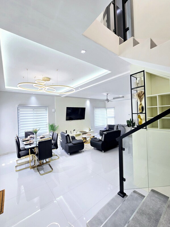 Una sala de estar moderna con comedor, una escalera y un televisor montado en la pared.