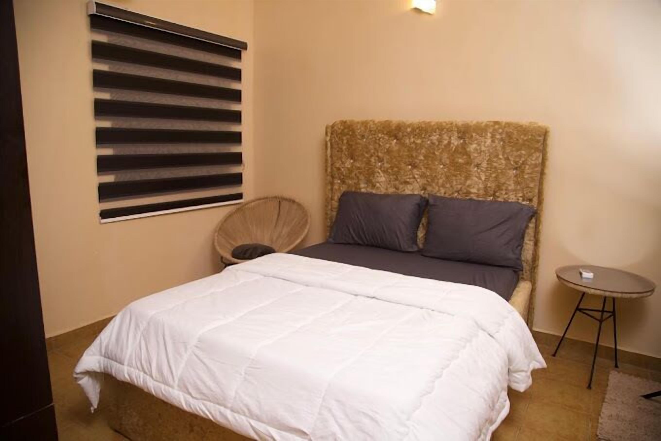 A bedroom with a bed, a headboard, a small round table, and a chair.