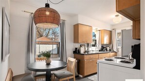 A modern kitchen with wooden cabinets, a white stove, and a dining area with a round table and chairs. - The Harlan City Cottage - Extended Stay Welcome (Grand Rapids)