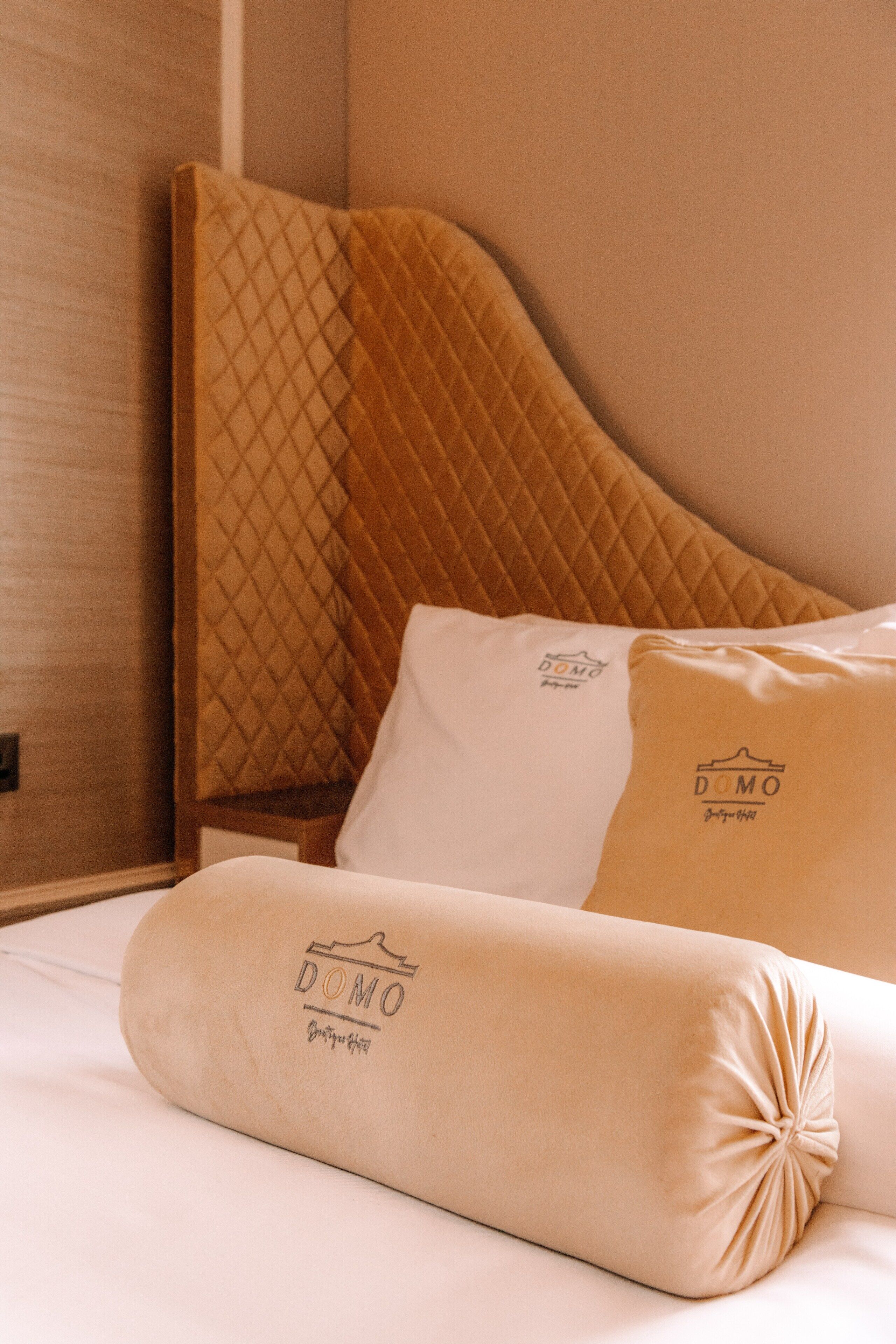 A bed with a quilted headboard, two pillows with a logo, and a neatly made bedspread.