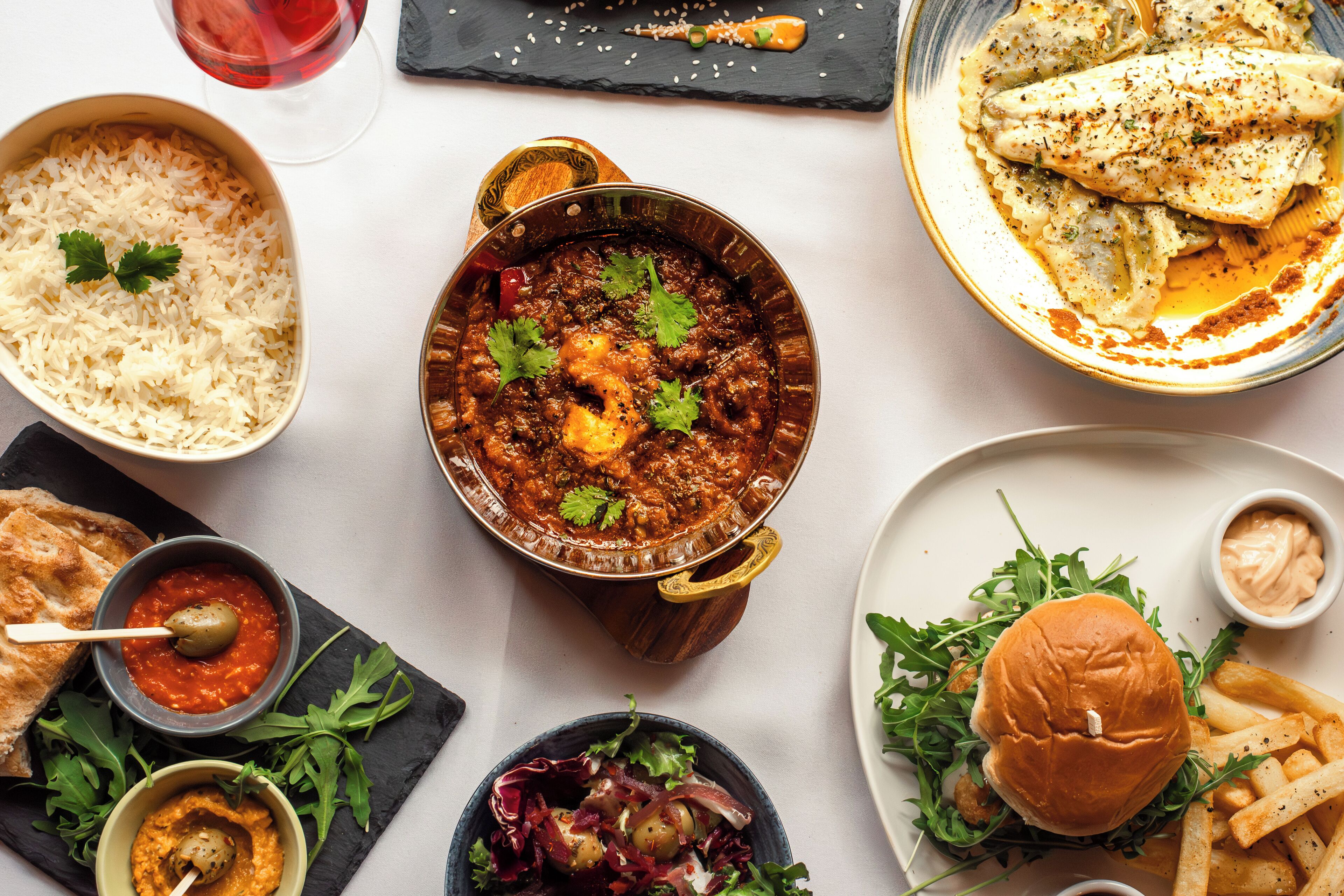 A variety of dishes including rice, a bowl of sauce, a salad, and a burger with fries.