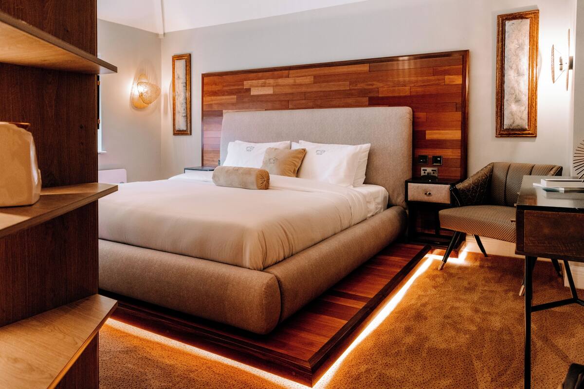 Une chambre d’hôtel moderne avec un grand lit, une tête de lit en bois, des tables de chevet et un bureau avec une chaise.