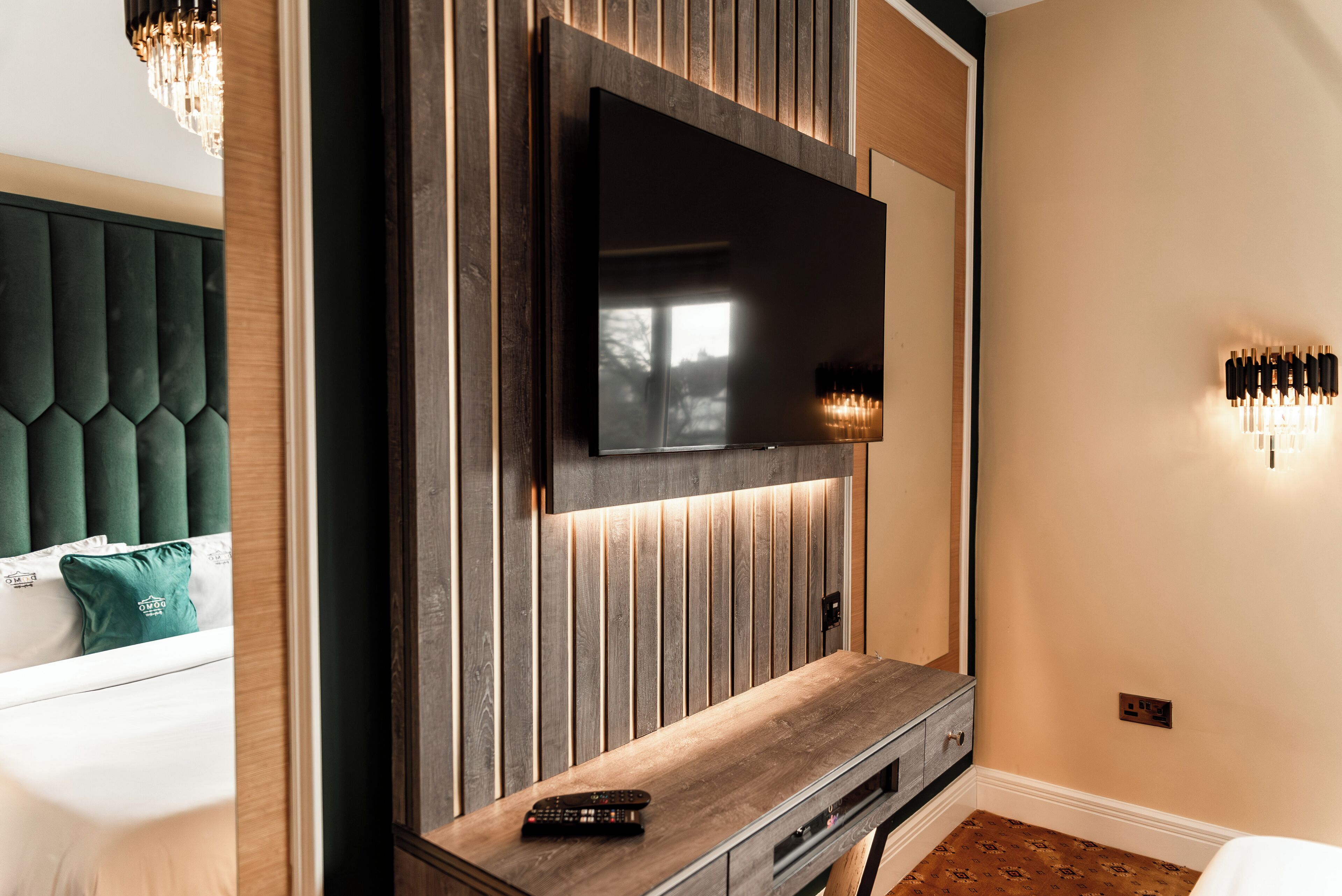 Una sala de estar moderna con un televisor de pantalla plana grande montado en una pared de madera, una mesa de centro de madera y un cabecero tapizado color verde.