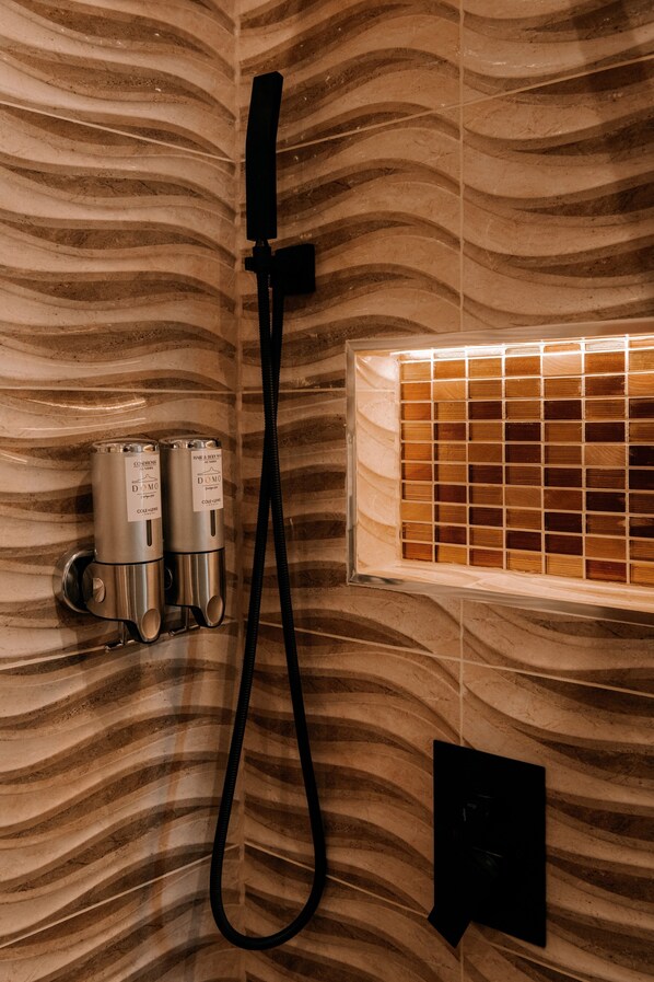 Un área de ducha con diseño de pared curva, un cabezal de ducha de mano y un cerramiento de vidrio.