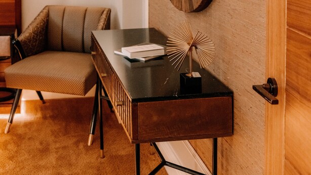 Ein modernes Interieur mit einer Holzwand, einem großen, ovalen Spiegel, einem dunklen Holzkonsole und einem gemusterten Sessel.