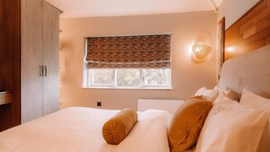 Ein Schlafzimmer mit einem großen Bett, einem Fenster mit einem gemusterten Rollo, einer Wandleuchte und einem Holzschrank.