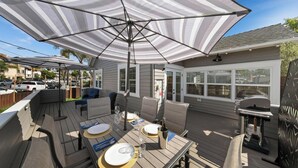 Une terrasse couverte, aménagée avec du mobilier d’extérieur, un barbecue et offrant une vue sur le quartier.