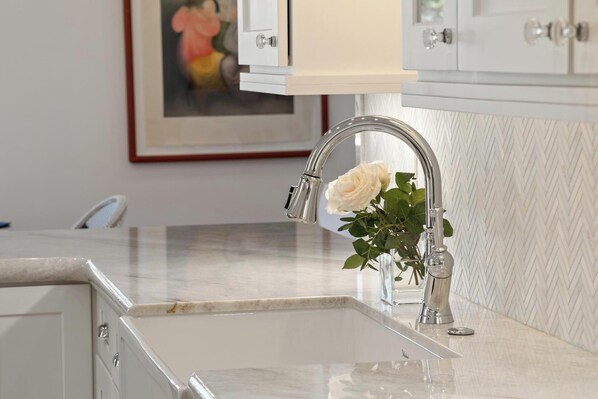 A kitchen sink with a modern faucet, a vase with a white rose, and a framed picture on the wall.