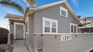 Une maison de plain-pied avec un revêtement extérieur gris, une porte d’entrée blanche et le numéro « 1287 » affiché sur le côté.