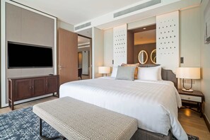 A modern hotel room with a large bed, a flat-screen TV, a wooden cabinet, and a decorative wall panel.