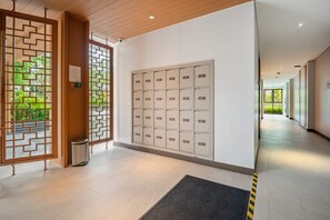 Een gang met een rij genummerde kasten, een houten deur met een geometrisch patroon en een prullenbak.