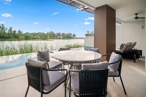 A poolside area with a round table and chairs, a ceiling fan, and a view of a lake.