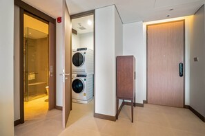 A hotel room with a glass shower, a washing machine, and a wooden cabinet.