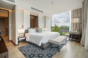 A modern hotel room with a large bed, bedside tables, a bench, and a view of the outdoors.