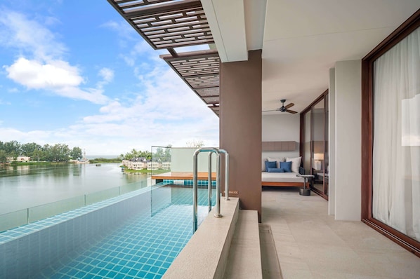 A modern hotel room with a glass balcony overlooking a swimming pool and a river.