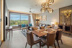 A spacious dining area with a large table set for six, a sofa with blue cushions, and a view of greenery through large windows.