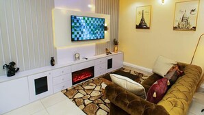 A modern living room with a flat-screen TV, a fireplace, a sofa, and decorative wall art. - The Panache Luxury Apartment (Lagos)