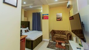 A compact hotel room with a bed, a sofa, a small table, and a TV. - The Panache Luxury Apartment (Lagos)