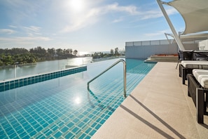 Una piscina infinita en la azotea con vistas despejadas al horizonte, una sombrilla y sillas de descanso.
