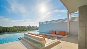 A modern outdoor pool area with a glass balustrade, beige sofas with orange cushions, and a clear view of the surrounding landscape. - Angsana Oceanview Residences, Two-Bedroom 162 C Penthouse (Choeng Thale)