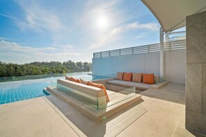 Un espace piscine extérieur moderne, doté d’une balustrade en verre, de canapés beige avec des coussins orange, et offrant une vue dégagée sur le paysage environnant.