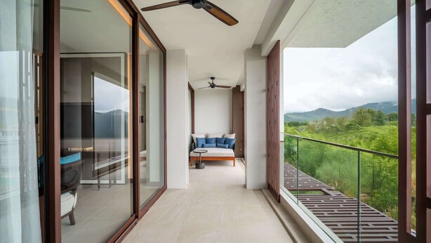 A balcony with a sofa and a table, a ceiling fan, and a view of greenery and mountains. - Angsana Oceanview Residences, Two-Bedroom 162 C Penthouse (Choeng Thale)