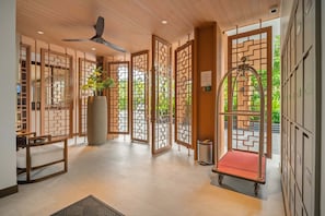 A hotel lobby with traditional wooden partitions, a ceiling fan, a reception desk, and a red trolley.