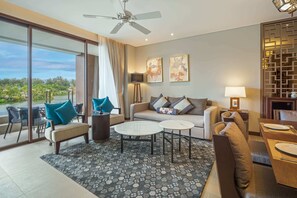 A spacious living area with a sofa, two coffee tables, and a dining table set for four. Large windows offer a view of a lake and greenery.