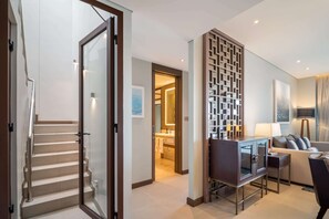 A modern living room with a glass staircase, a flat-screen TV, a sofa, and a decorative wall panel.