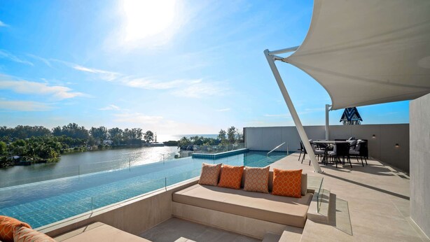 A rooftop pool area with a view of a river, outdoor seating, and a dining area.