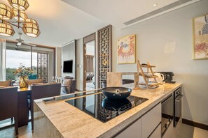 A modern kitchen with a glass cooktop, a dining area with a table and chairs, and a large window offering a view of the outdoors. - Angsana Oceanview Residences, Two-Bedroom 164 Cc Penthouse (Choeng Thale)