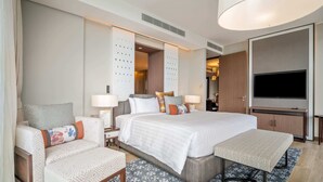 A modern hotel room with a large bed, a desk, a chair, a TV, and a wardrobe.