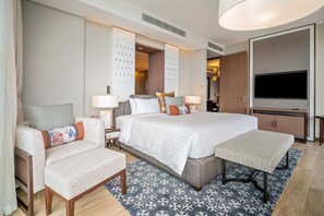 A modern hotel room with a large bed, a desk, a chair, a TV, and a wardrobe.