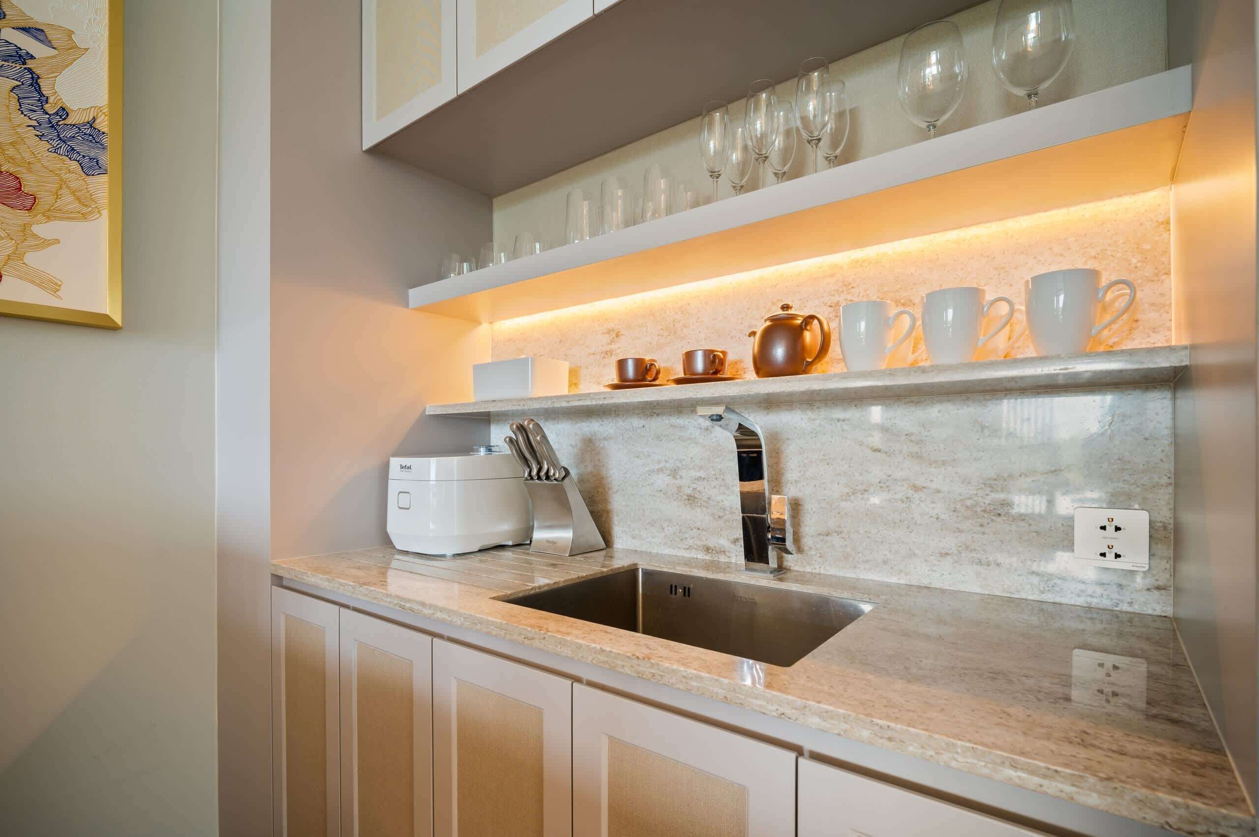 Cozinha moderna com bancada de mármore, pia de aço inoxidável e uma estante com copos e taças.