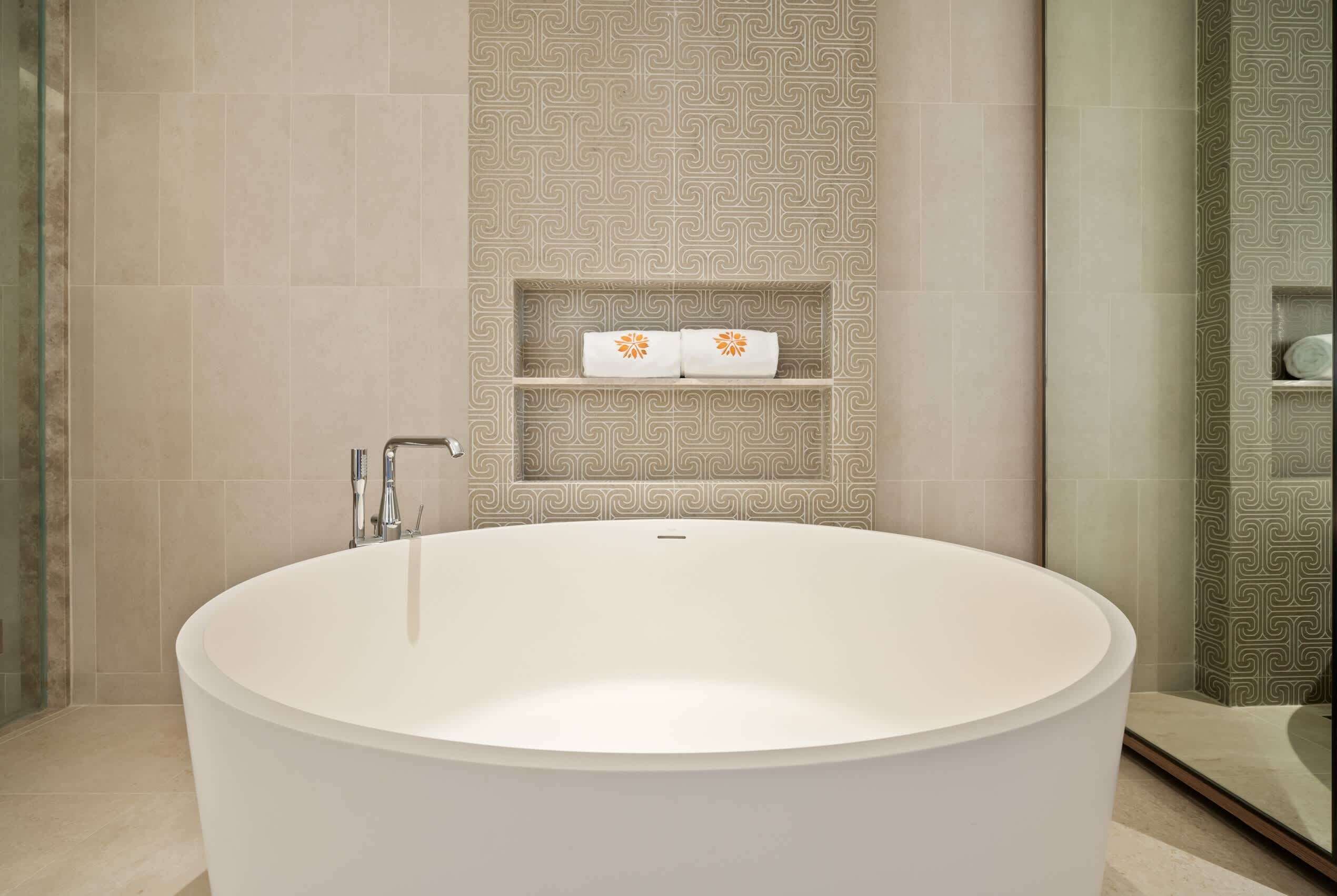 A modern bathroom with a large freestanding bathtub, a glass shower enclosure, and patterned wall tiles.