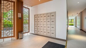 A hallway with a row of numbered lockers, a wooden door with a geometric pattern, and a trash bin.