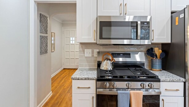 A modern kitchen with white cabinetry, a stainless steel stove, a microwave, and a refrigerator. - Soak and Play: Hot Tub + Family Arcade Fun (Euclid)