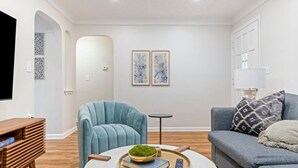 A modern living room with a blue armchair, grey sofa, and a round coffee table with books and a remote control. - Soak and Play: Hot Tub + Family Arcade Fun (Euclid)