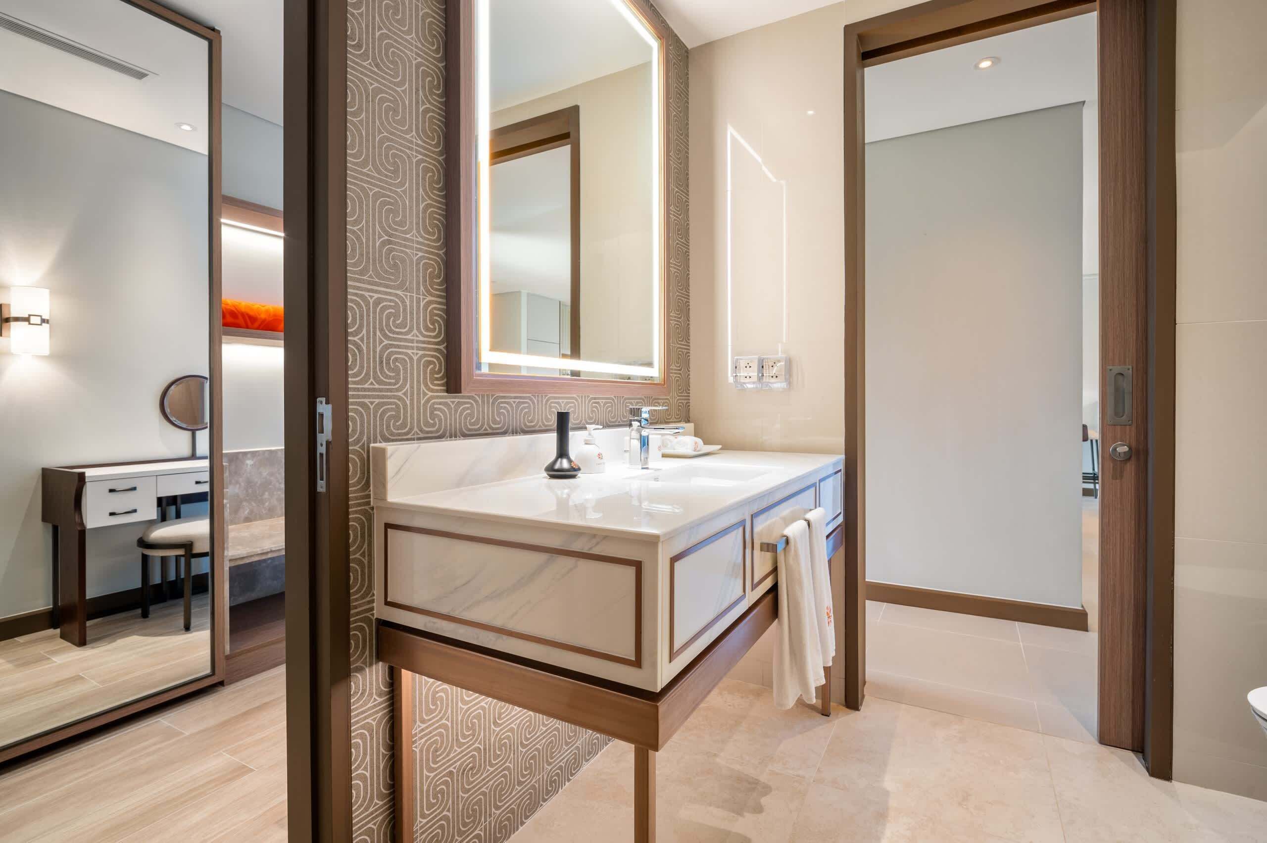 A modern bathroom with a large mirror, a marble sink, and a wooden vanity.