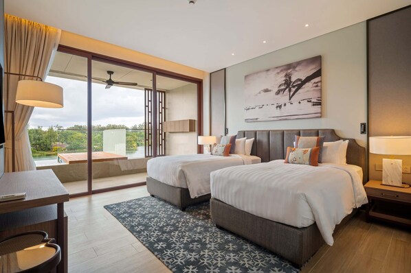 Habitación de hotel moderna con dos camas, un escritorio y un balcón con vistas a zonas verdes.