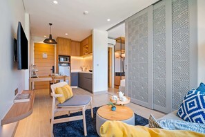 Un salon moderne comprenant un canapé, un fauteuil, une table basse et un téléviseur. Il y a également un coin cuisine avec des meubles en bois et un four à micro-ondes.