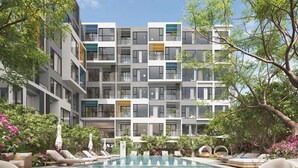 Een modern appartementencomplex met een zwembad, lounge fauteuils en weelderige beplanting.