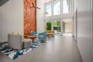 Un hall d’entrée moderne avec un canapé gris aux lignes courbes, des fauteuils bleus et un tapis à motifs.