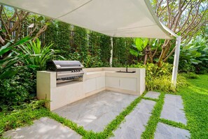 Een moderne buitenkeuken met een ingebouwde grill, omringd door weelderige begroeiing en een pad van natuursteen.
