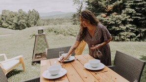 A woman at an outdoor wooden table with white bowls and wine glasses, surrounded by wicker chairs and a pergola. - 2-Level Home • Tremblant Mountain View • Fireplace (Mont-Tremblant)