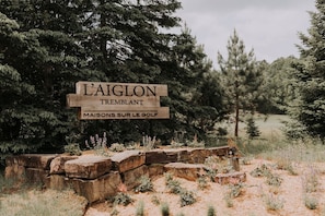 A wooden sign with 'L'AIGLON TREMBLANT' and 'MAISONS SUR LE GOLF' text, set against a backdrop of trees and a stone wall.