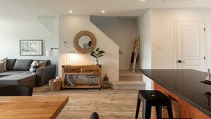 A modern living space with a sofa, wooden dining table, kitchen area, and staircase. - 2-Level Home • Tremblant Mountain View • Fireplace (Mont-Tremblant)
