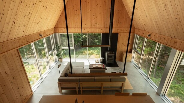 Interior de una cabaña de madera con sofá, mesa de comedor y chimenea.