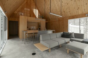 Et moderne interiør med træloft, en grå modulsofa og et køkkenområde.